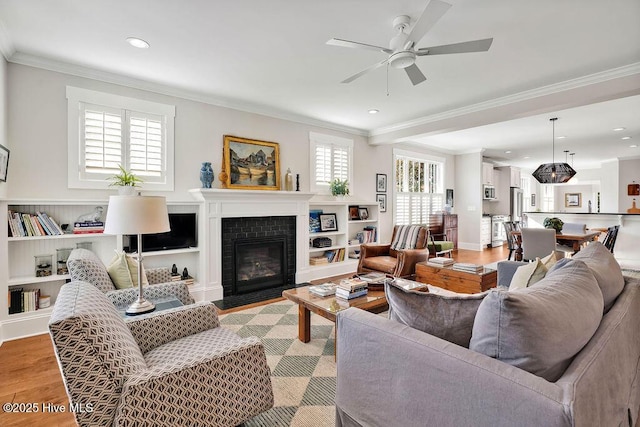 living room with ceiling fan, light hardwood / wood-style floors, ornamental molding, and a fireplace