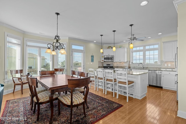 dining space with sink, ornamental molding, ceiling fan with notable chandelier, and light wood-type flooring