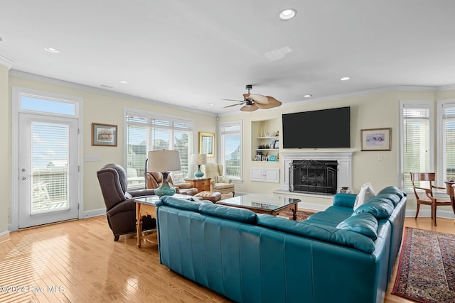 living room featuring ceiling fan, built in features, ornamental molding, and light wood-type flooring