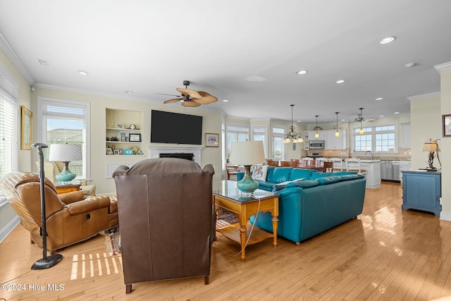 living room with plenty of natural light, light hardwood / wood-style floors, built in features, and crown molding