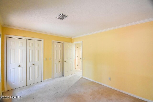 unfurnished bedroom with light carpet, ornamental molding, and multiple closets