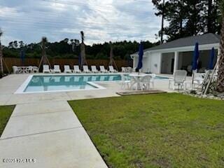 community pool with a patio area, a lawn, and an outbuilding