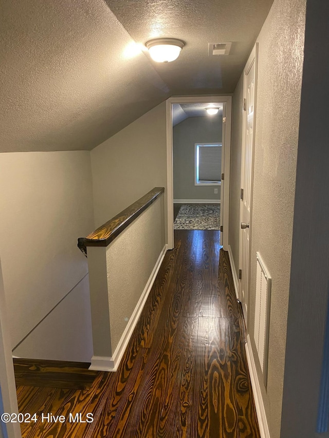 hallway with a textured ceiling, dark hardwood / wood-style floors, and lofted ceiling