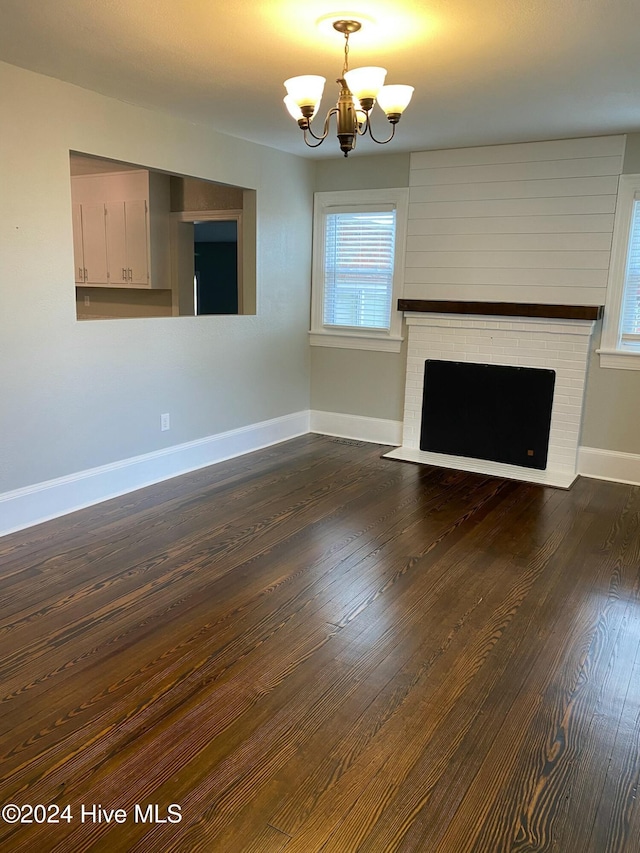 unfurnished living room with dark hardwood / wood-style floors, an inviting chandelier, and a brick fireplace