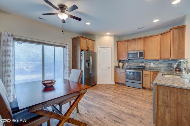 kitchen with light stone countertops, sink, stainless steel appliances, light hardwood / wood-style floors, and decorative backsplash