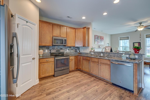 kitchen featuring dark stone counters, sink, ceiling fan, appliances with stainless steel finishes, and light hardwood / wood-style floors