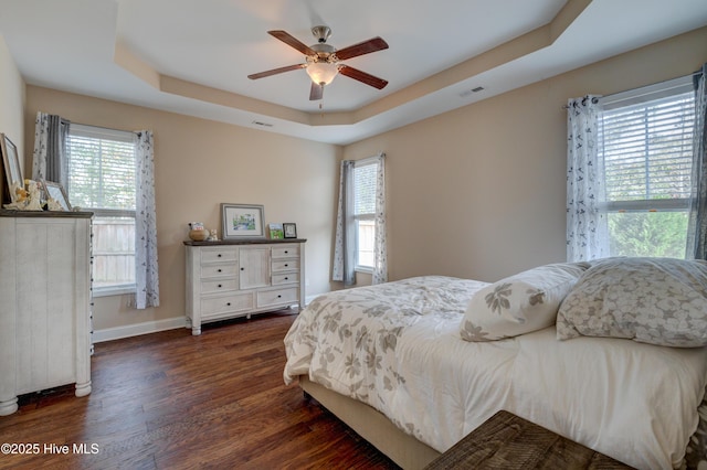 bedroom with a raised ceiling, ceiling fan, and dark wood-type flooring