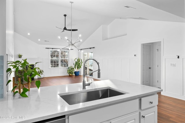 kitchen with light stone countertops, sink, hanging light fixtures, vaulted ceiling, and white cabinets