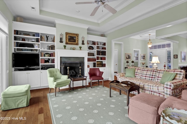 living room featuring hardwood / wood-style flooring, ceiling fan, ornamental molding, and a tray ceiling