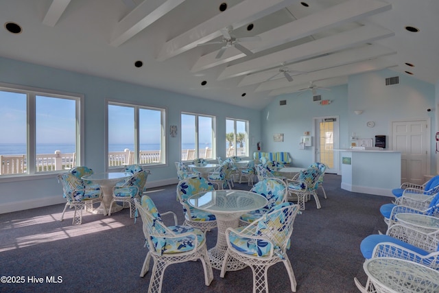 dining space with beamed ceiling, dark colored carpet, a water view, and a wealth of natural light