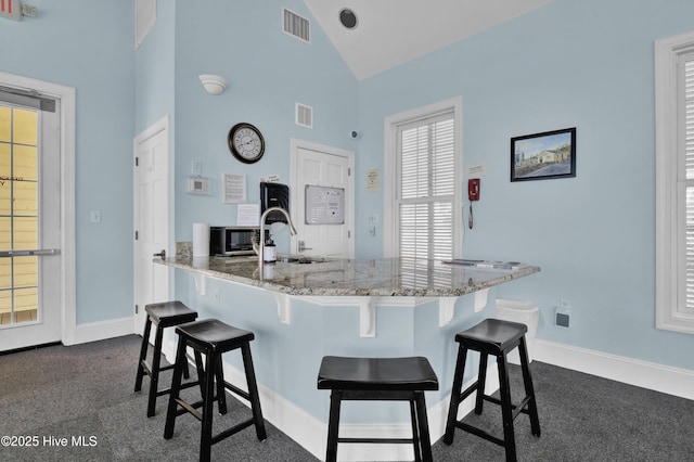 kitchen with a breakfast bar area, light stone countertops, and visible vents