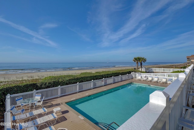 community pool with a beach view, a water view, and fence