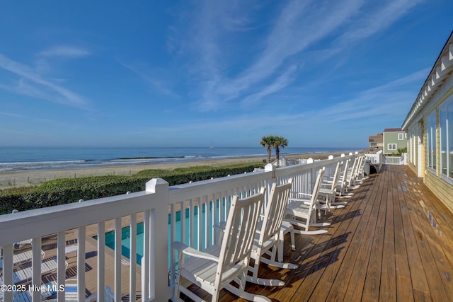 deck with a fenced in pool, a water view, and a view of the beach