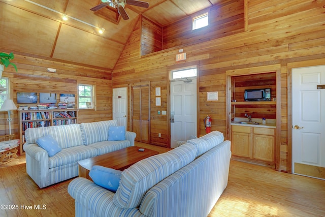 living area featuring wooden walls, high vaulted ceiling, light wood-type flooring, and ceiling fan