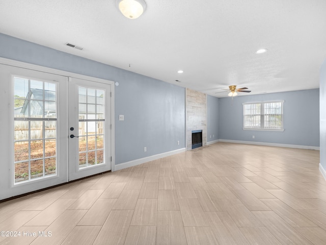 unfurnished living room with a textured ceiling, ceiling fan, a fireplace, and french doors