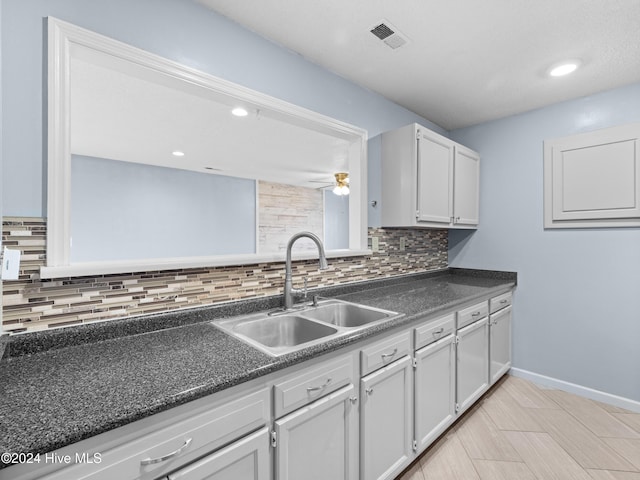 kitchen with tasteful backsplash, ceiling fan, sink, and white cabinets