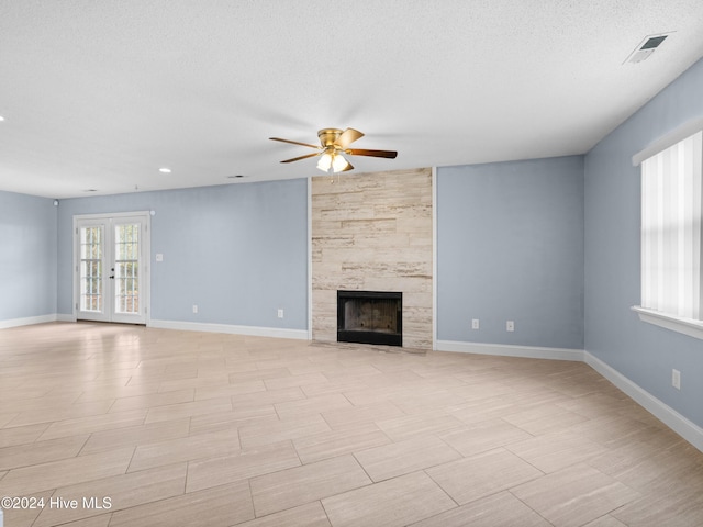 unfurnished living room featuring a tiled fireplace, ceiling fan, french doors, and a textured ceiling