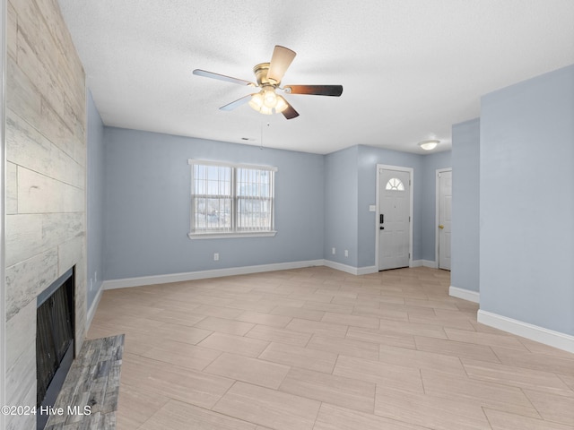 unfurnished living room featuring a tiled fireplace, ceiling fan, and a textured ceiling