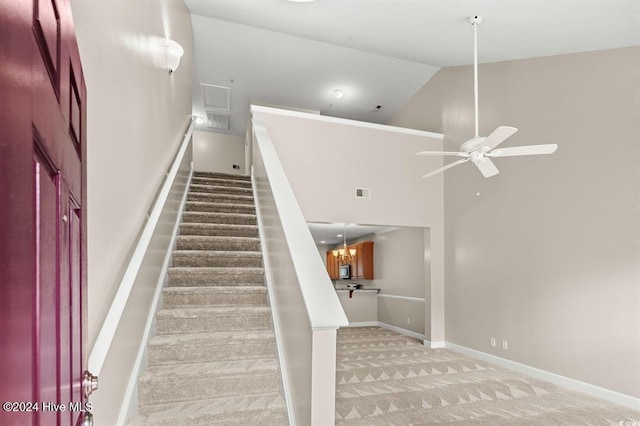 stairs with carpet flooring, ceiling fan with notable chandelier, and high vaulted ceiling