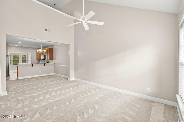 carpeted spare room featuring ceiling fan with notable chandelier and high vaulted ceiling