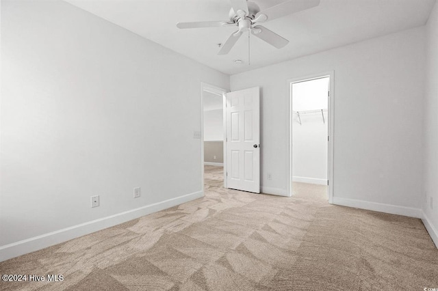 unfurnished bedroom featuring a walk in closet, ceiling fan, a closet, and light colored carpet