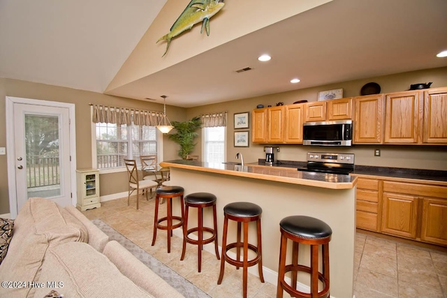 kitchen with vaulted ceiling, decorative light fixtures, a kitchen bar, a kitchen island with sink, and appliances with stainless steel finishes