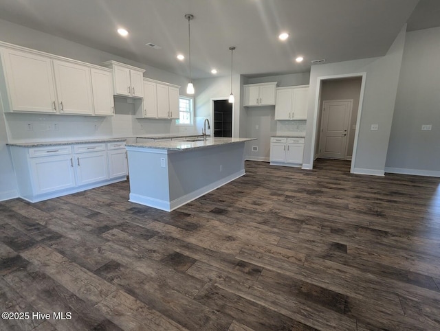 kitchen featuring dark hardwood / wood-style floors, a kitchen island with sink, white cabinets, hanging light fixtures, and light stone counters