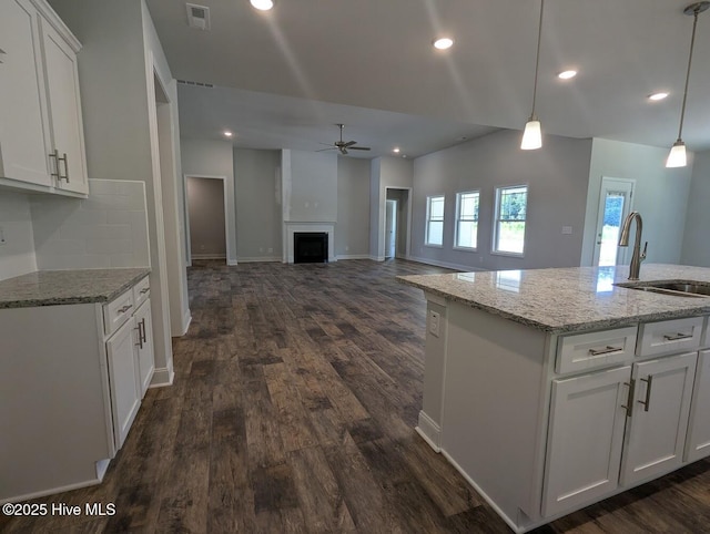 kitchen featuring ceiling fan, a kitchen island with sink, hanging light fixtures, white cabinets, and sink