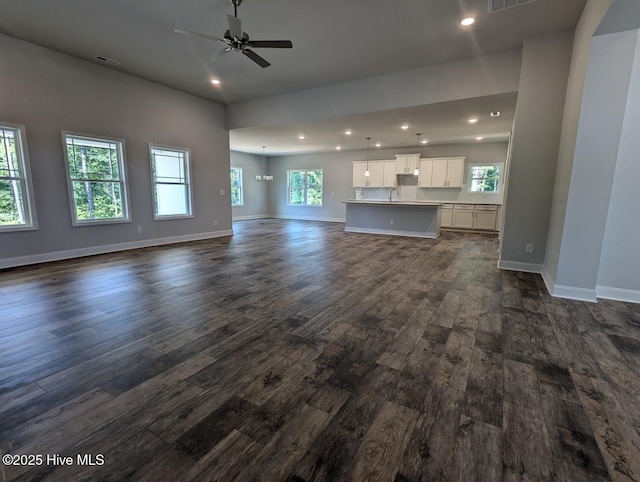 unfurnished living room featuring dark hardwood / wood-style flooring, a wealth of natural light, and ceiling fan with notable chandelier