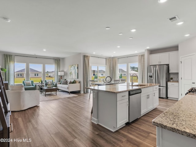 kitchen with light stone countertops, stainless steel appliances, sink, a center island with sink, and white cabinetry