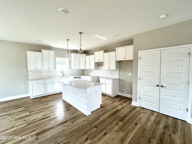 kitchen with dark wood-type flooring, a kitchen island, a sink, and backsplash