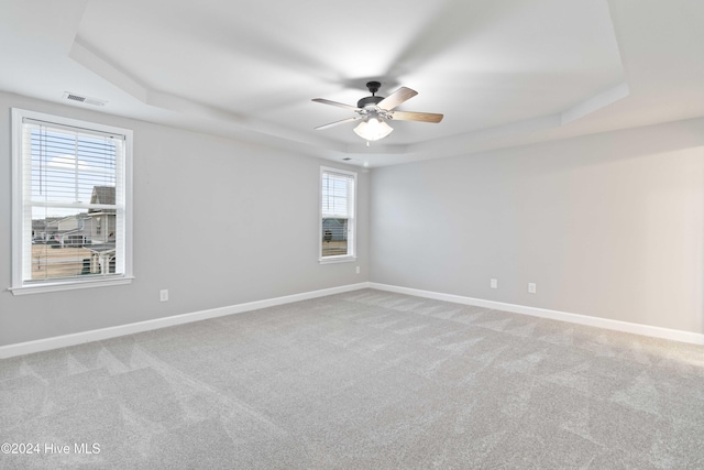 carpeted spare room featuring a raised ceiling, ceiling fan, and a healthy amount of sunlight