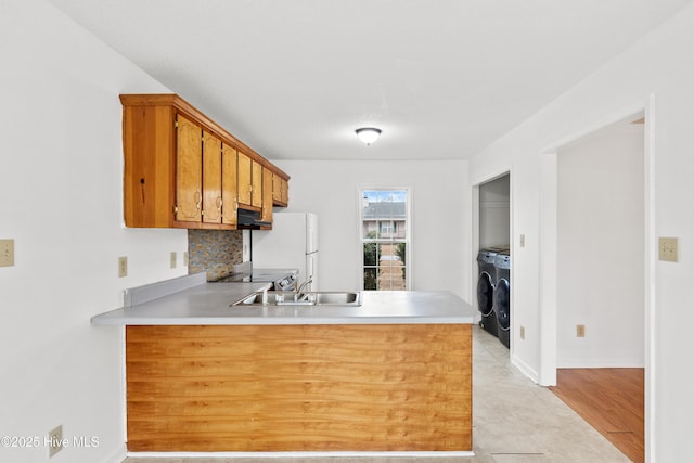 kitchen with white refrigerator, washing machine and clothes dryer, sink, and kitchen peninsula