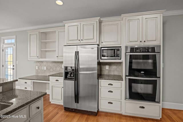 kitchen with dark stone countertops, light hardwood / wood-style flooring, stainless steel appliances, ornamental molding, and white cabinets