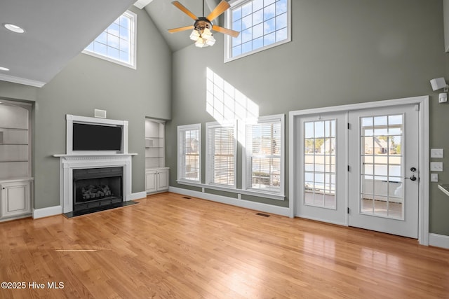 unfurnished living room with light hardwood / wood-style floors, a high ceiling, built in shelves, and ceiling fan