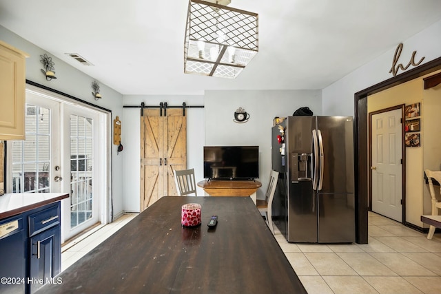 kitchen with dishwashing machine, light tile patterned floors, stainless steel refrigerator with ice dispenser, a barn door, and blue cabinetry