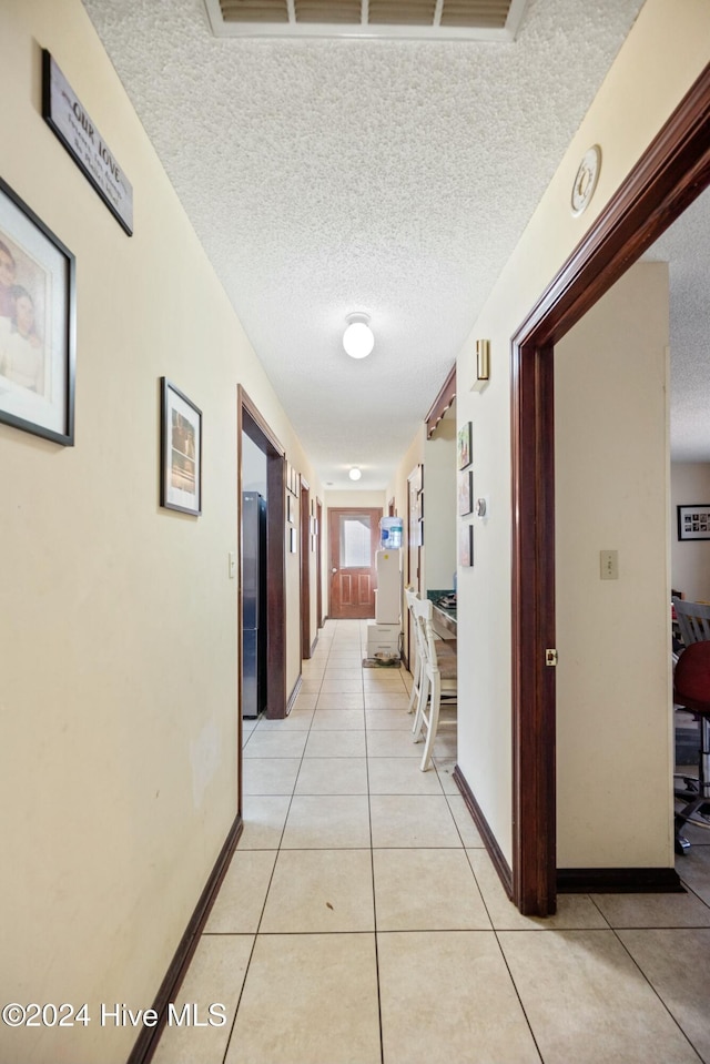 hallway featuring light tile patterned flooring, elevator, and a textured ceiling