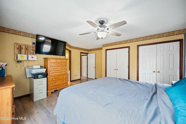 bedroom featuring multiple closets, wood-type flooring, a textured ceiling, and ceiling fan