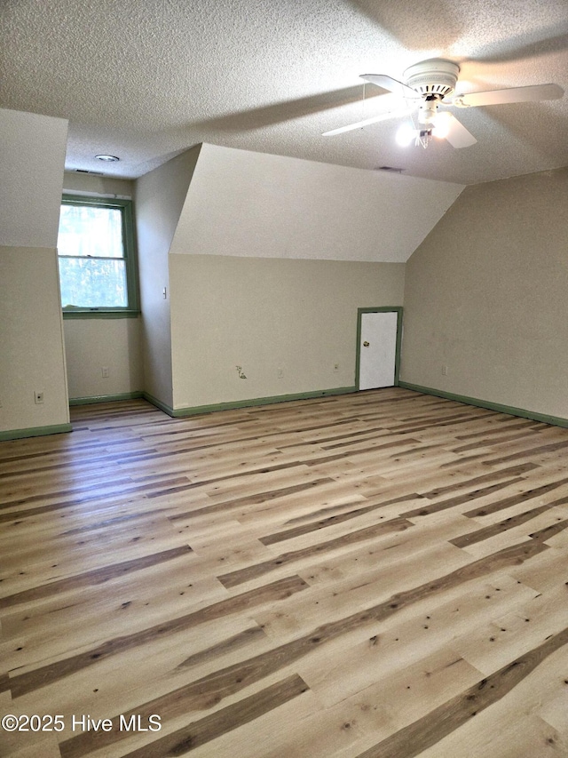 additional living space with a textured ceiling, vaulted ceiling, ceiling fan, and light wood-type flooring