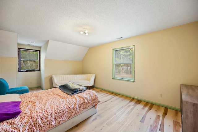 bedroom featuring lofted ceiling, a textured ceiling, and light hardwood / wood-style floors