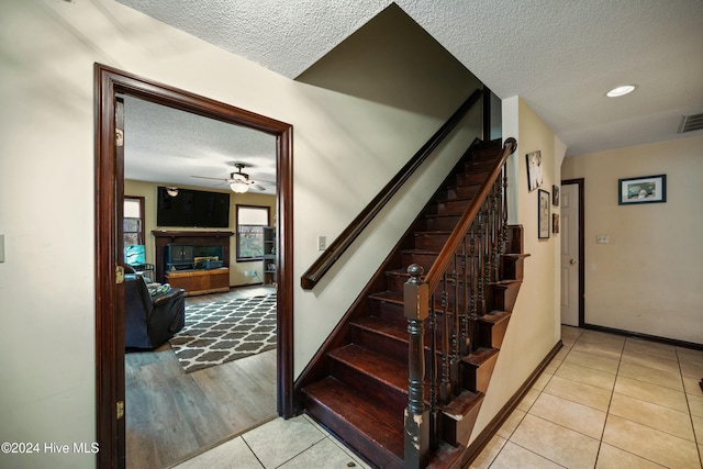 stairway with ceiling fan, tile patterned floors, and a textured ceiling