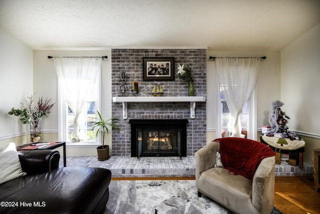 living room featuring plenty of natural light, hardwood / wood-style floors, a textured ceiling, and a brick fireplace