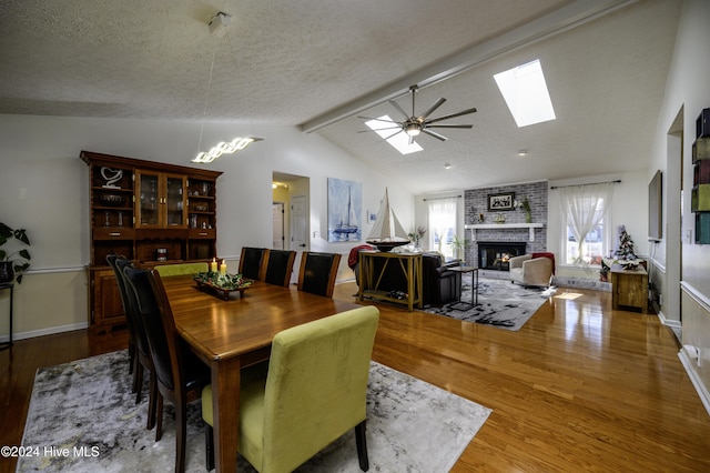 dining room with a brick fireplace, a textured ceiling, lofted ceiling with skylight, ceiling fan, and hardwood / wood-style floors