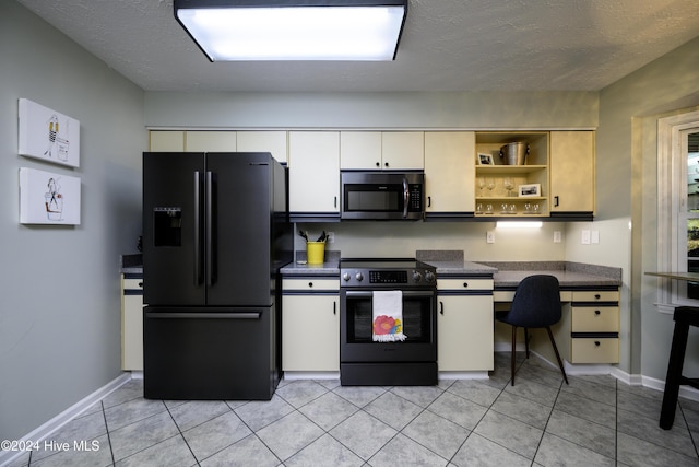 kitchen with electric stove, black fridge, white cabinets, and light tile patterned flooring