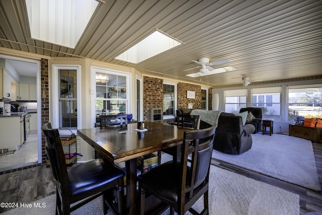 dining room featuring hardwood / wood-style floors, ceiling fan, brick wall, and a skylight