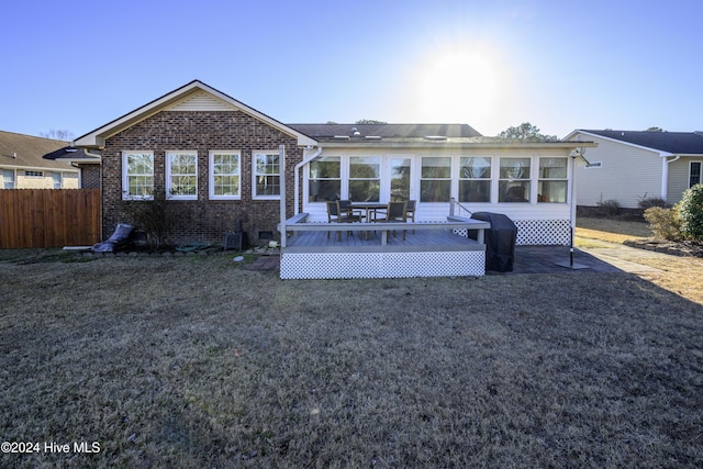 rear view of property featuring a lawn, a sunroom, and a deck