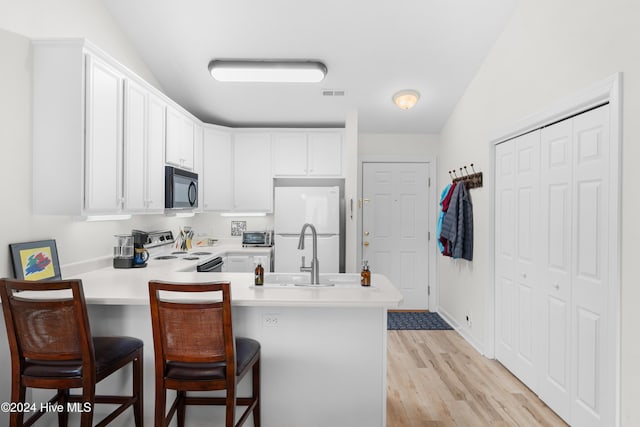 kitchen with white fridge, kitchen peninsula, range with electric cooktop, and white cabinetry