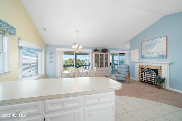 kitchen with lofted ceiling, an inviting chandelier, a fireplace, white cabinets, and light colored carpet