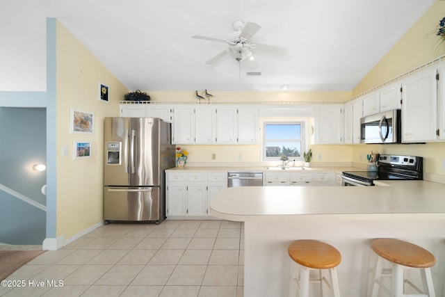 kitchen featuring a breakfast bar, appliances with stainless steel finishes, white cabinets, vaulted ceiling, and kitchen peninsula