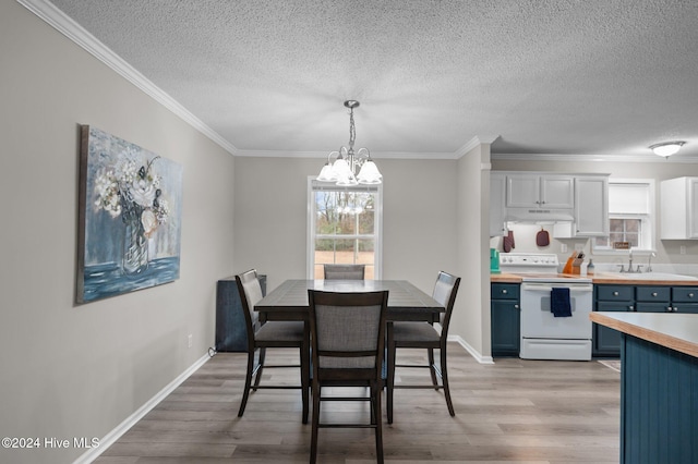 dining room with a textured ceiling, ornamental molding, light wood-type flooring, and an inviting chandelier